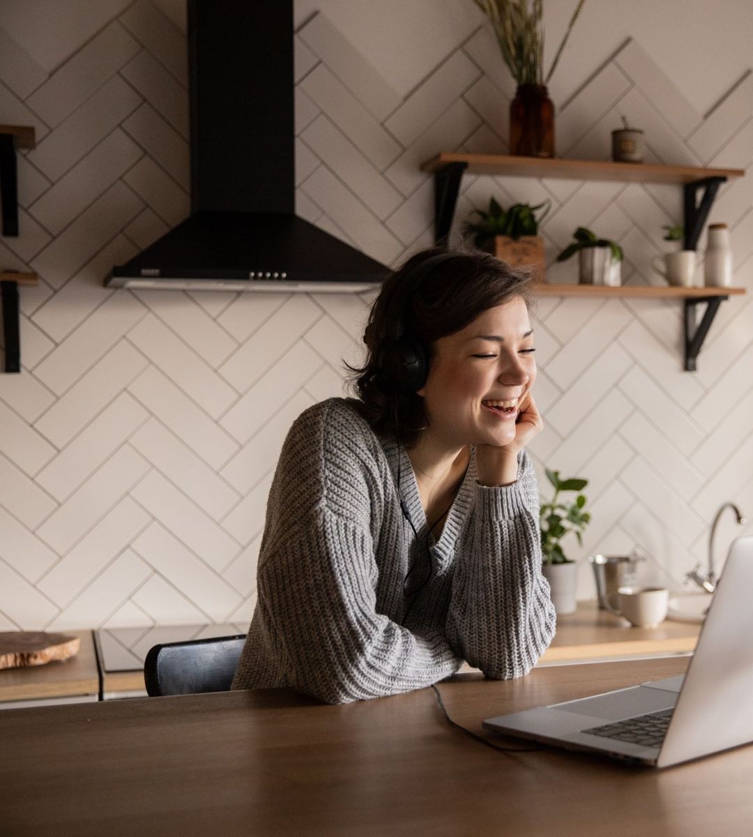Woman smiling during a video call on her laptop at a kitchen table